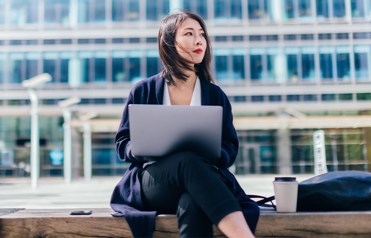 Young woman sitting outside with a laptop looking away.